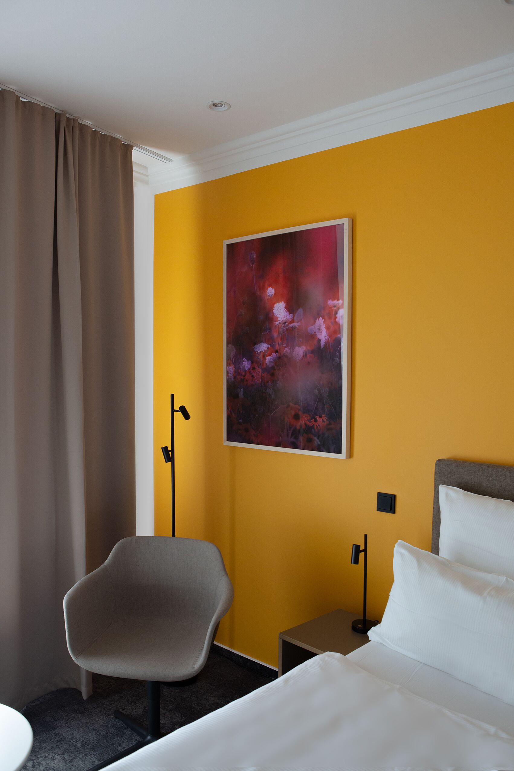 A hotel room with a bed, a chair, a nightstand, and a painting on the wall.