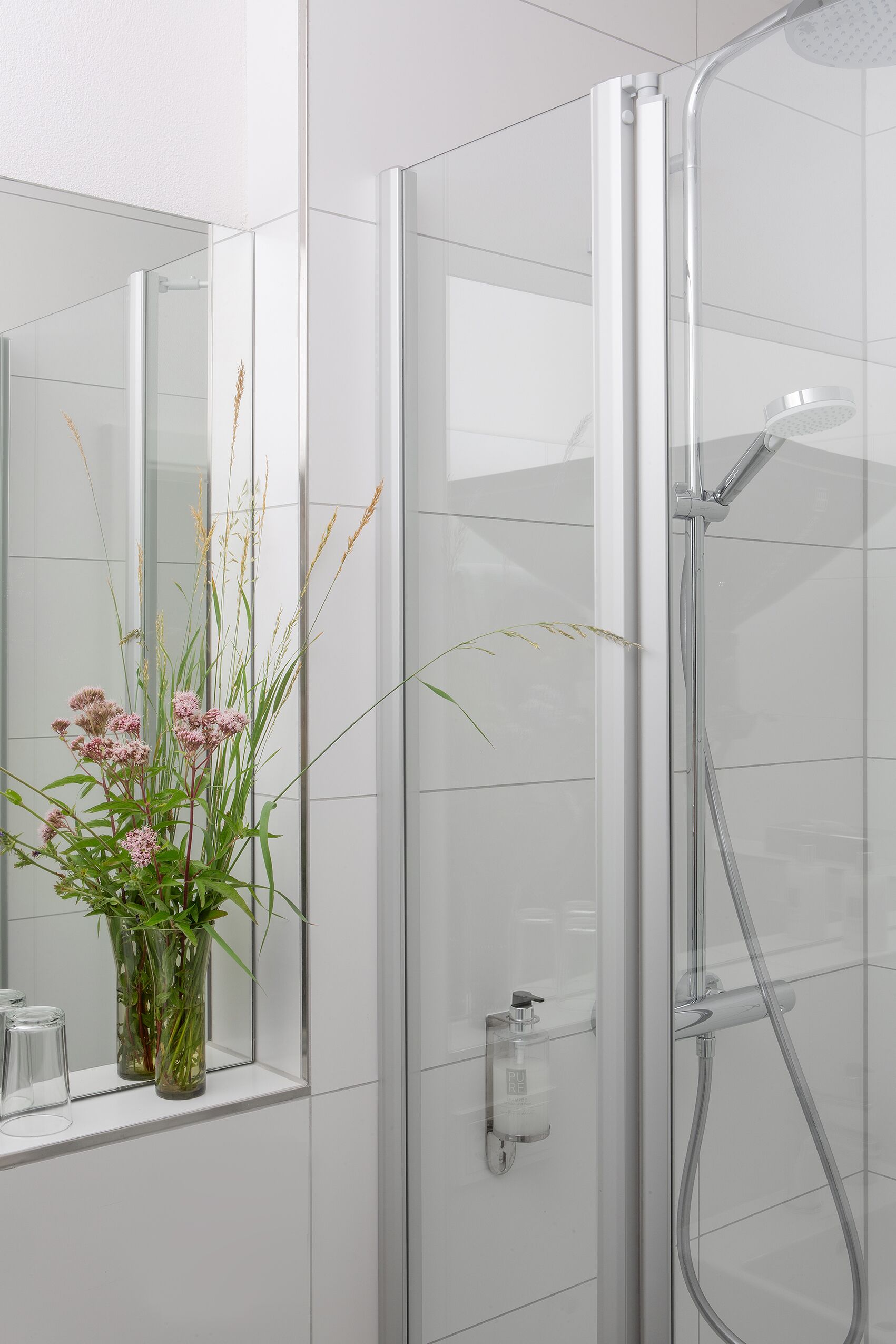A modern bathroom with a glass shower enclosure, a mirror, and a vase with flowers on the sink.