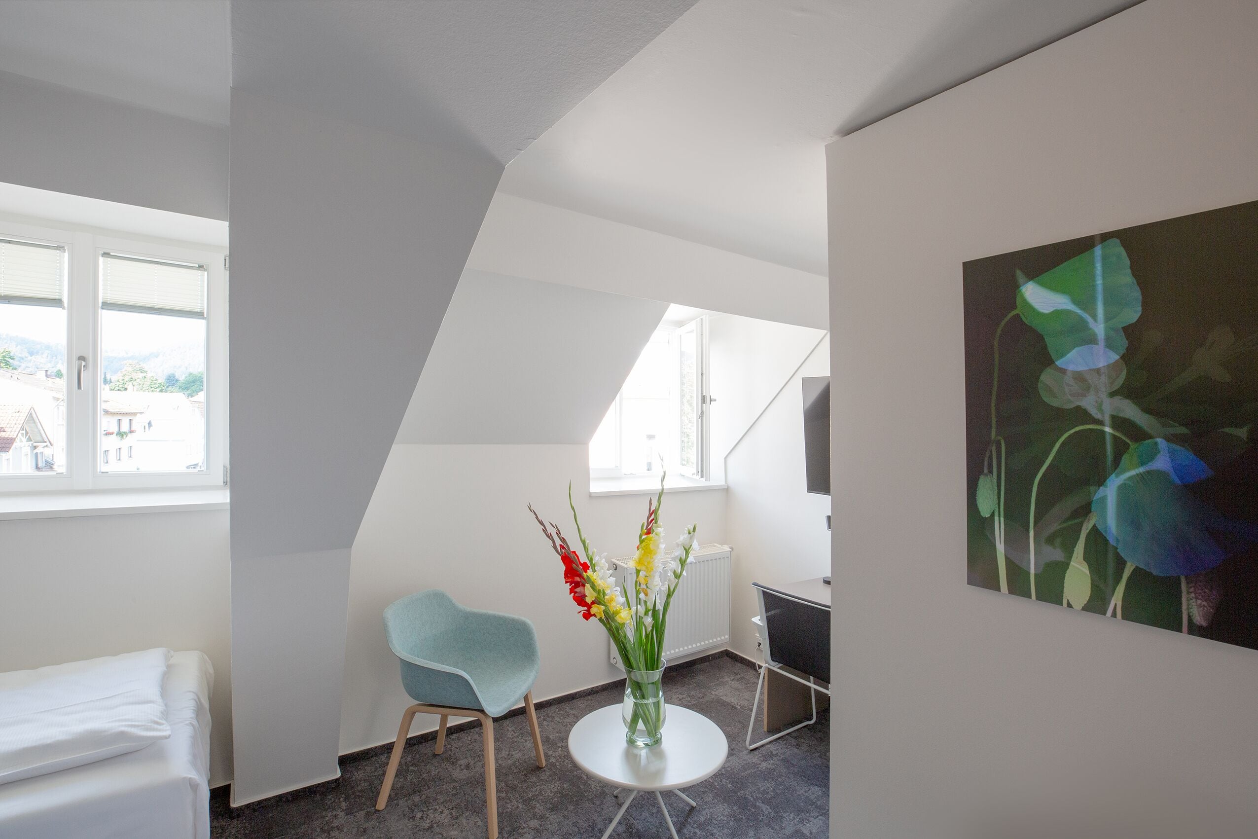 A modern room with a bed, a chair, a desk, and a window with a view.