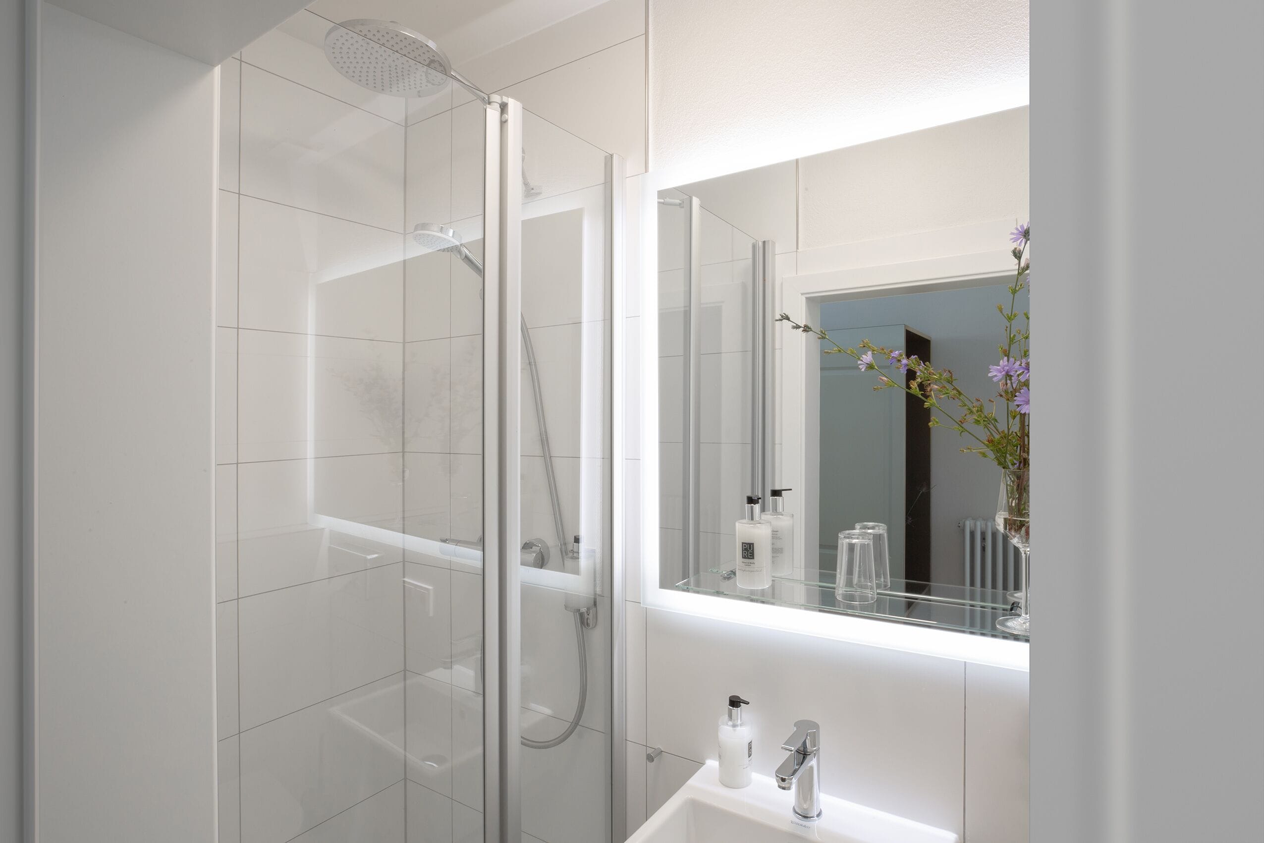 Une salle de bain moderne avec une douche à parois de verre, un lavabo blanc et un miroir au-dessus du lavabo.