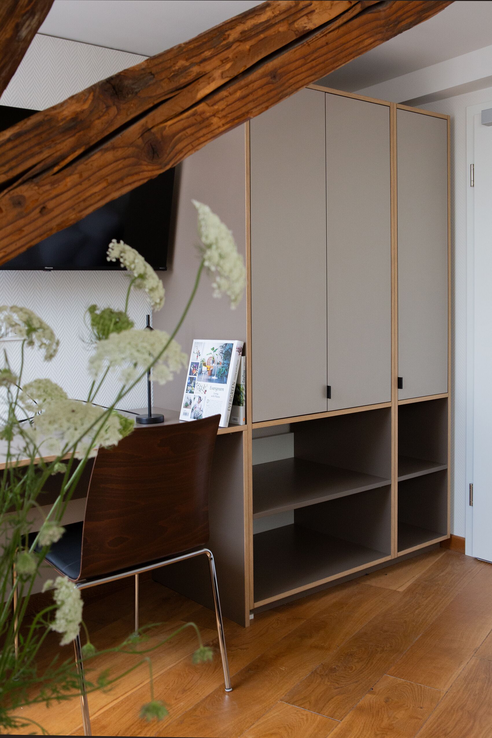 Een kamer met een houten bureau, een stoel, een boekenplank en een aan de muur bevestigde televisie.