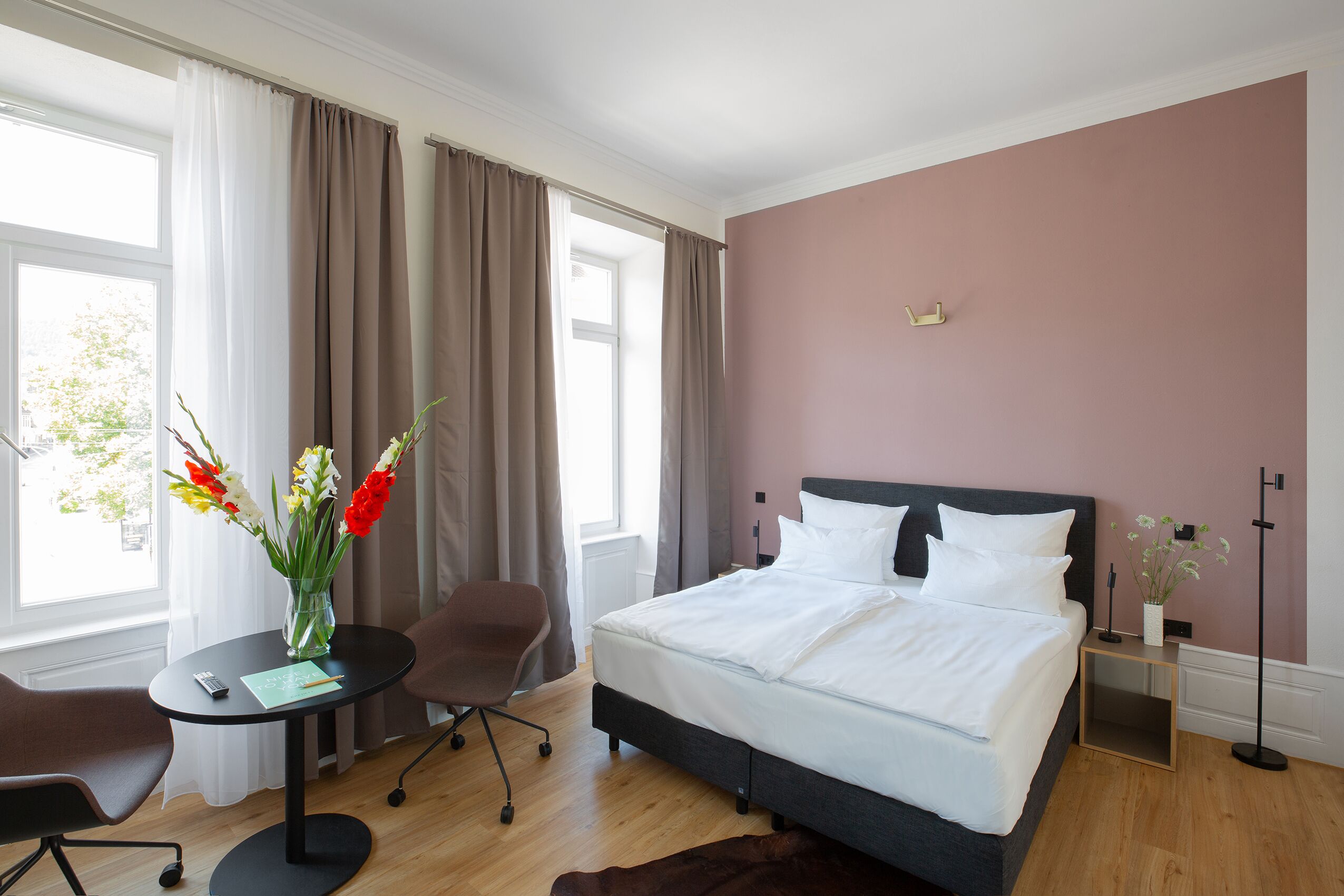 Ett hotellrum med en säng, ett skrivbord, en stol och ett fönster med gardiner.