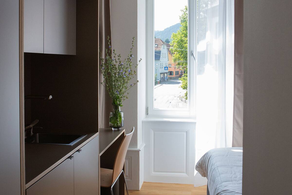 A bedroom with a bed, a desk, and a window with curtains.