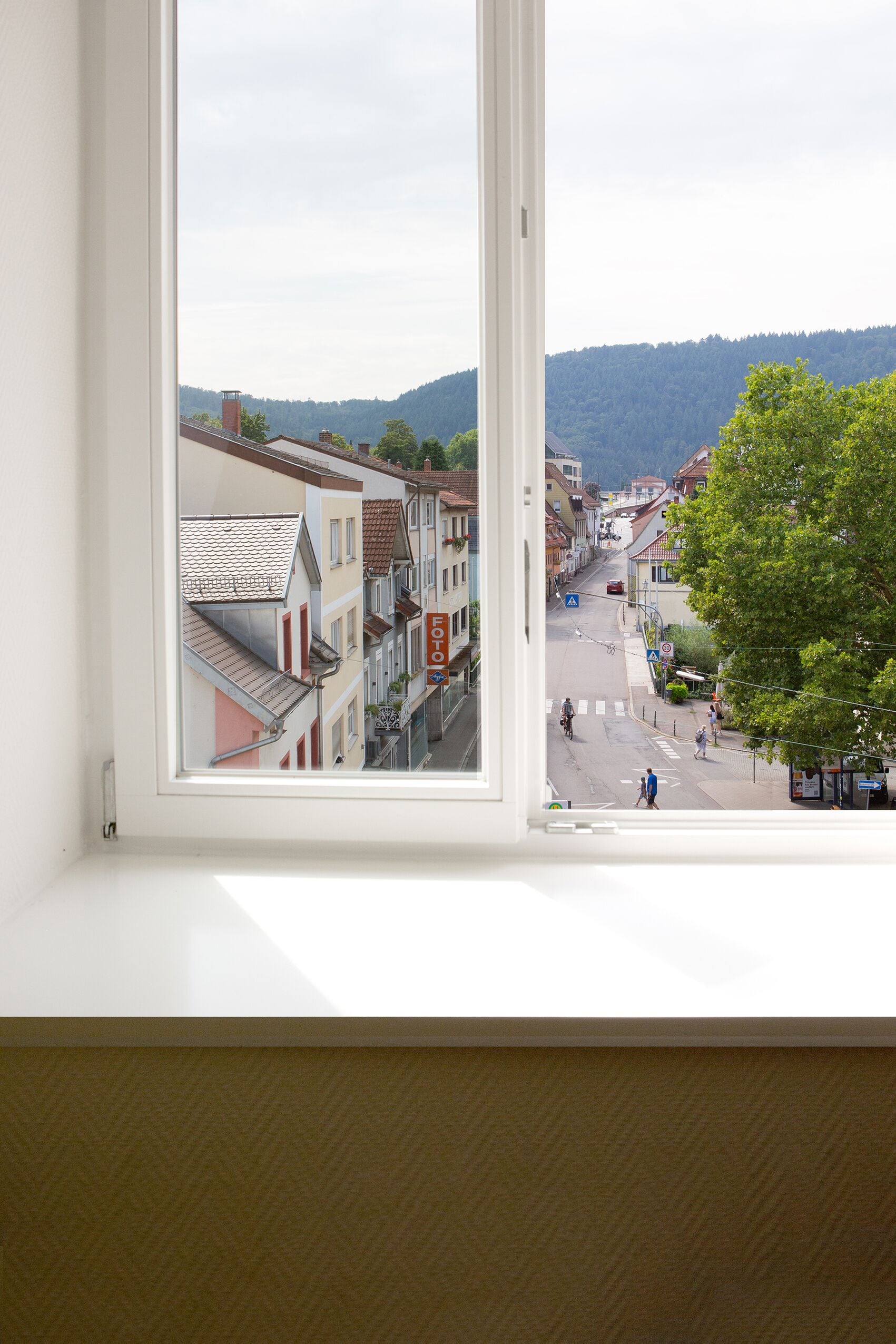 A view from a window overlooking a street with buildings, a tree, and a hilly landscape in the distance.
