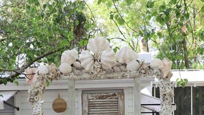 A white house with a porch covered in seashells, a wooden door, and potted plants. - North End, 3 Br Luxury Cottage, Pet Friendly, Private Road, 5 min walk to Beach (Tybee Island)