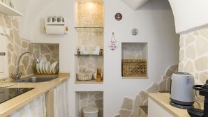 Una cocina con pared de piedra, un fregadero, una cafetera y estantes con utensilios de cocina.