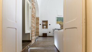 Un pasillo estrecho, con una pared de piedra a un lado y una puerta blanca al otro.