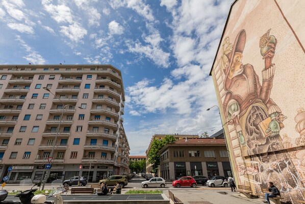 A multi-story building with a flat facade, a street with parked cars, and a mural on the right side.