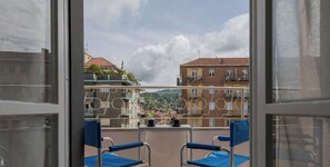 Een balkon met twee blauwe stoelen en een tafel, met uitzicht op een woongebied met gebouwen en een heldere lucht.