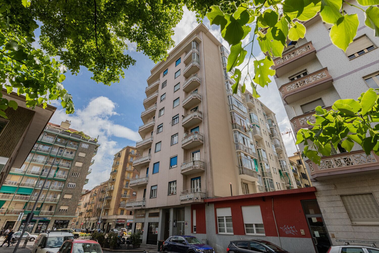 En flervåningsbyggnad med bostäder, balkonger, en butikslokal på markplan och parkerade bilar.