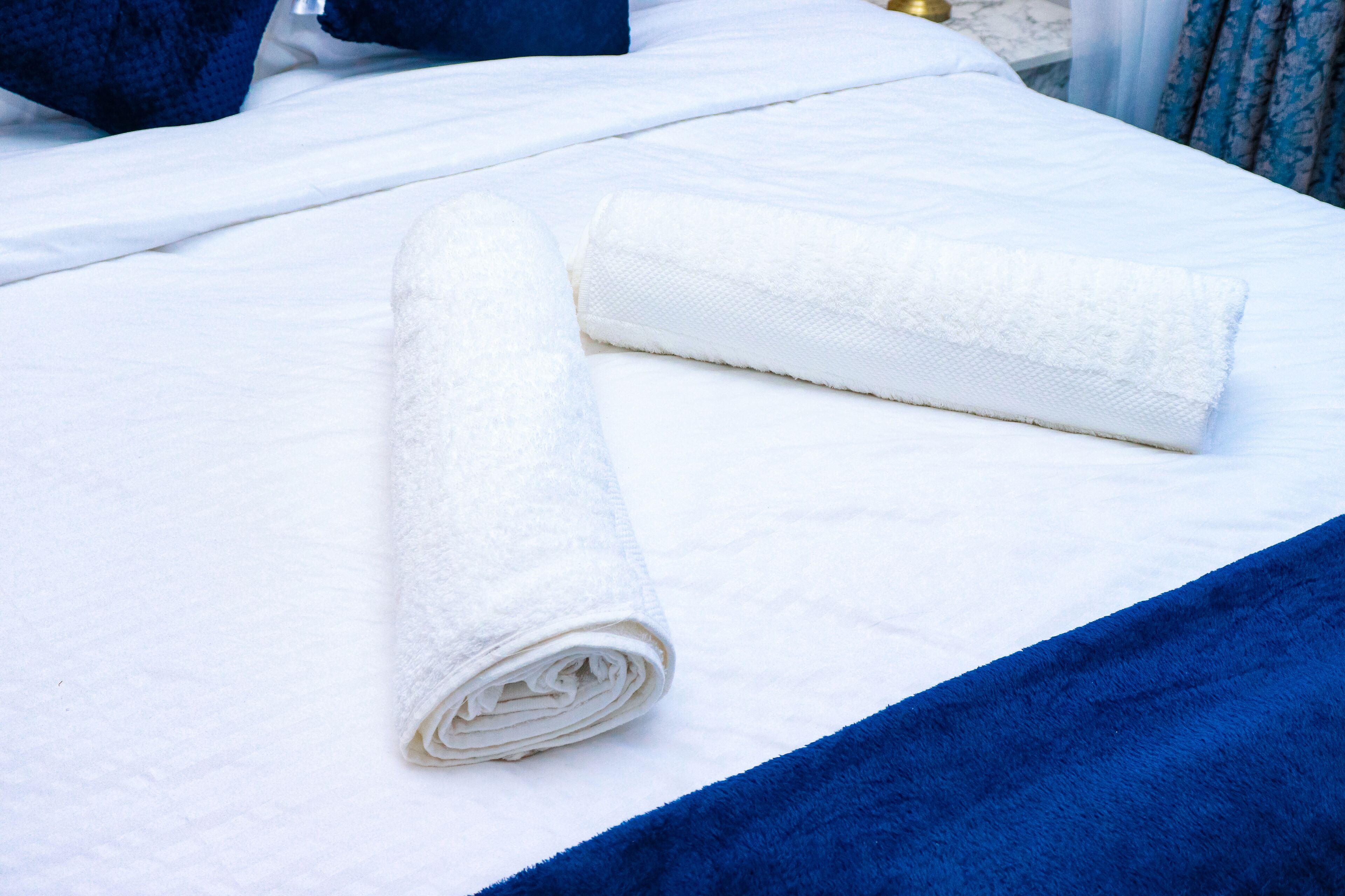 Een net opgemaakt bed met een witte handdoek en een blauwe deken.