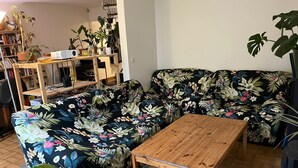 A living room with a floral sofa, a wooden coffee table, and a bookshelf filled with books and decorative items.