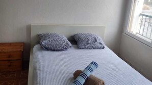 A bedroom with a bed, two pillows, a wooden nightstand, and a window.