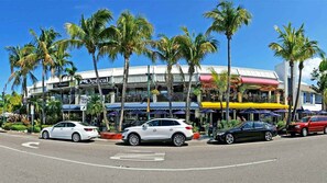 A hotel with a modern design, featuring a prominent 'Optical' sign, palm trees, and a street view with parked cars.