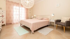 A bedroom with a bed, bedside tables, a chair, a dresser, and a hanging light fixture.
