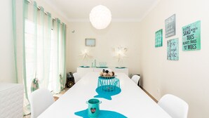 A dining area with a long table, teal placemats, and a white pendant light.
