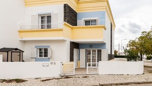 A two-story building with a yellow and white facade, a stone accent wall, and a gated entrance.