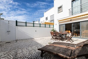 A patio with a table and chairs, a wooden lounge area, and a white building with a balcony. - 3 bedroom villa 50 metres from the beach with patio by AlgarveManta (15V3) (Manta Rota)