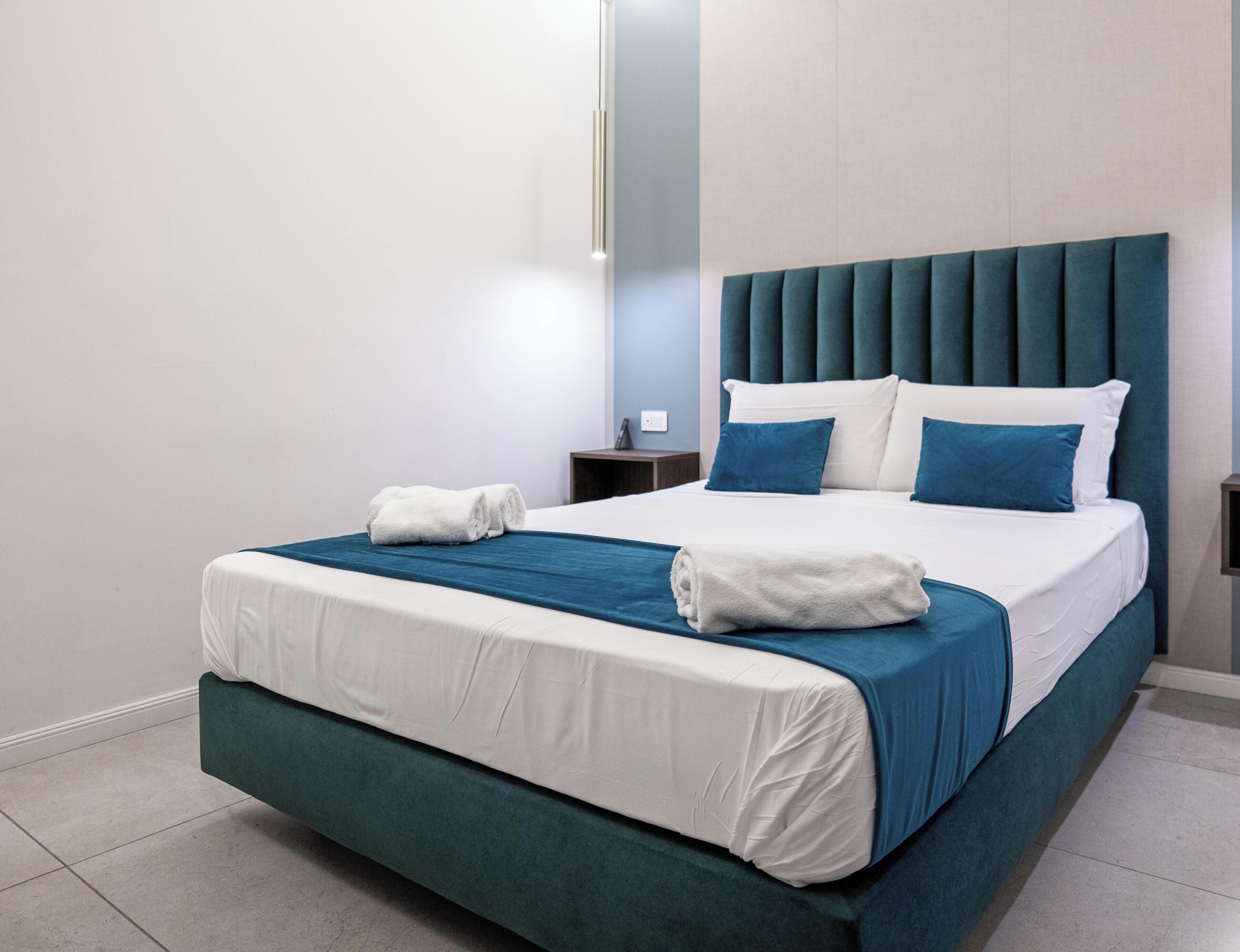 A modern hotel room with a large bed, two pillows, a bedside table, and a nightstand.