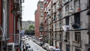 Una stretta via fiancheggiata da edifici a più piani, auto parcheggiate e balconi con panni stesi ad asciugare.