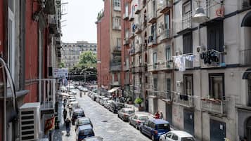 Uma rua estreita, flanqueada por edifícios altos, carros estacionados e varandas com roupas a secar.