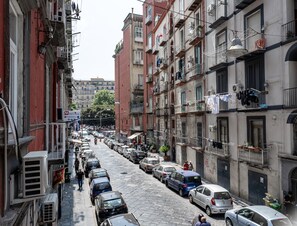 A narrow street lined with multi-story buildings, parked cars, and balconies with laundry hanging out to dry. - Museo Suite (Naples)