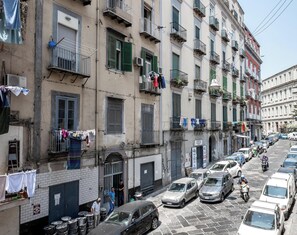 A narrow street lined with multi-story buildings, parked cars, and motorcycles. - Museo Suite (Naples)