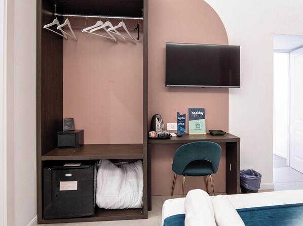 A hotel room with a bed, a desk with a flat-screen TV, a chair, a coat rack, a small kitchenette, and a sign indicating a holiday rate. - Museo Suite (Naples)