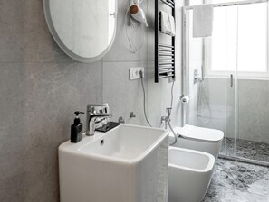 A modern bathroom with a large sink, two toilets, a shower, and a towel rack. - Museo Suite (Naples)