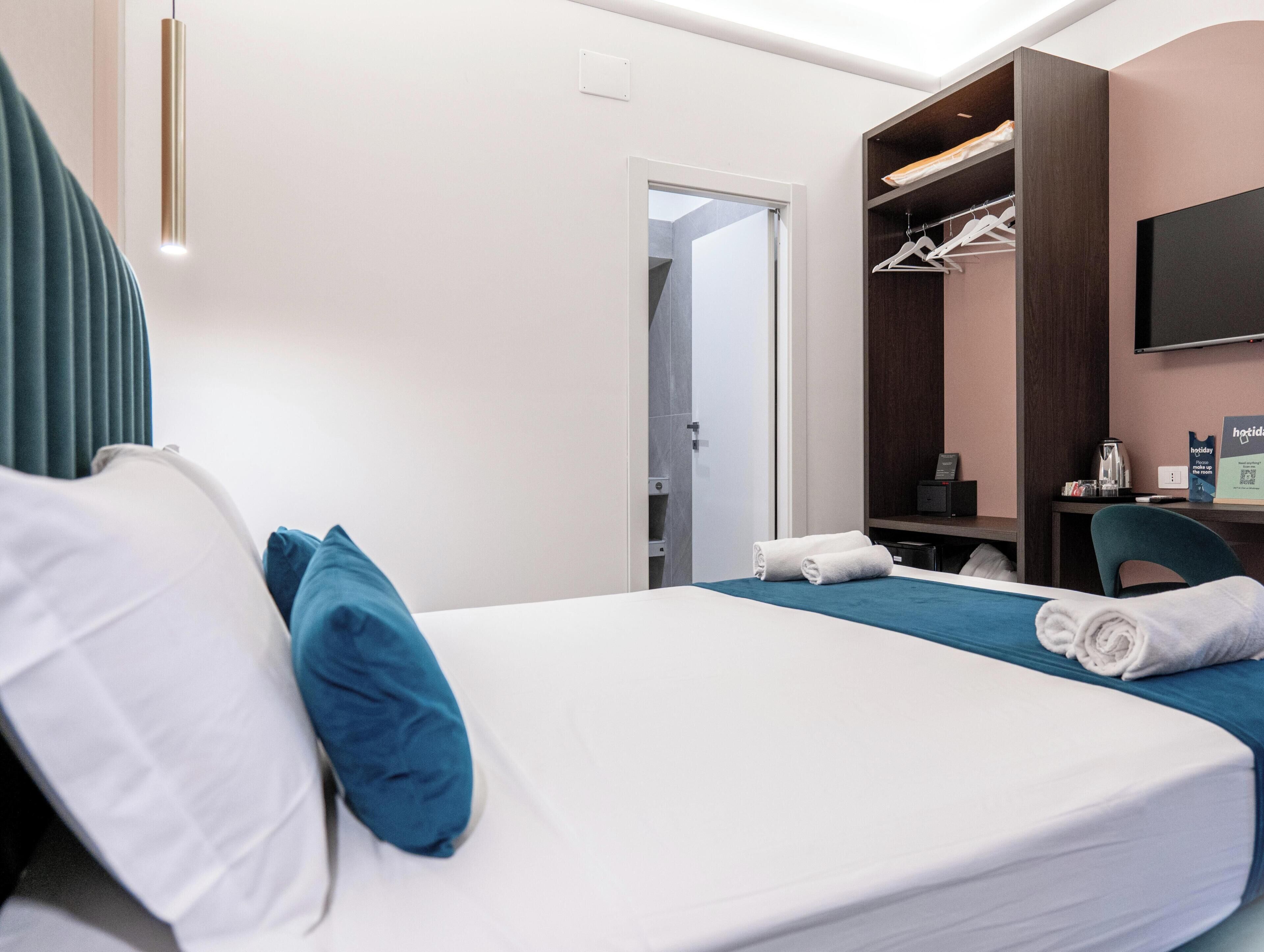 Una habitación de hotel con cama, escritorio, silla, armario y televisor.