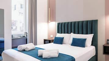 Quarto de hotel com cama, mesa de cabeceira, janela com cortinas e vista para prédios.