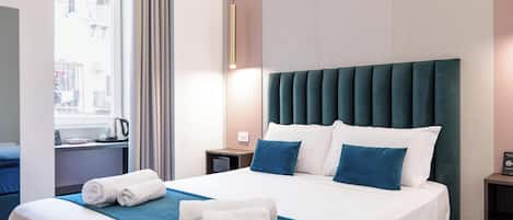 A hotel room with a large bed, a nightstand, a window with curtains, and a wall-mounted light fixture.
