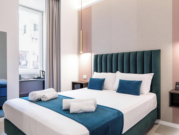 A hotel room with a large bed, a nightstand, a window with curtains, and a wall-mounted light fixture. - Museo Suite (Naples)