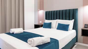 Quarto de hotel com cama, almofadas, mesa de cabeceira e luminária fixada na parede.