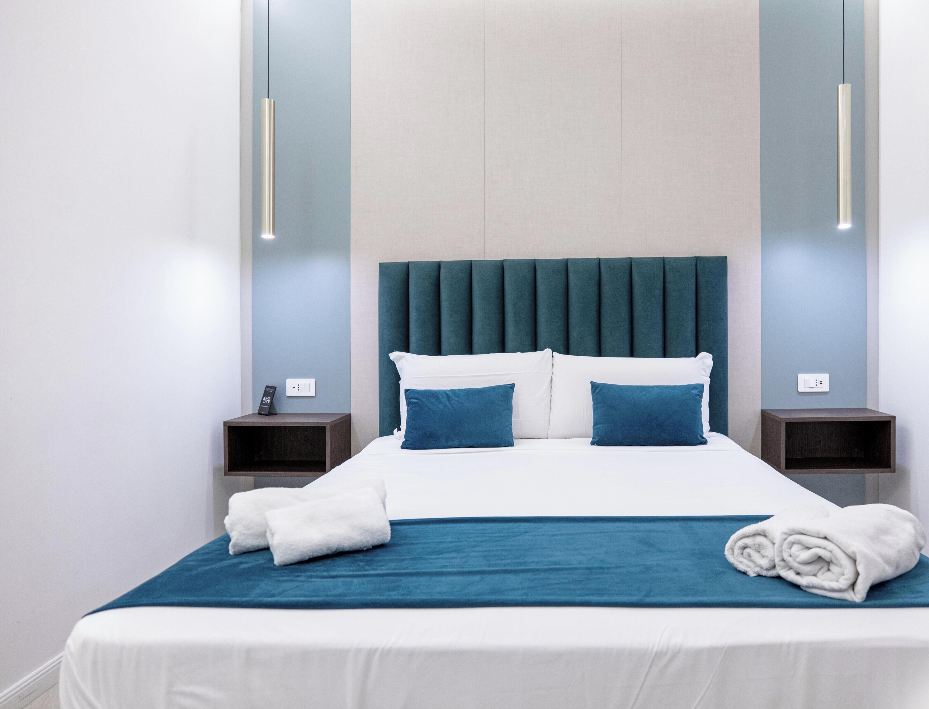 A neatly made bed with white and blue bedding, two bedside tables with lamps, and a headboard with vertical panels.
