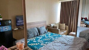 A hotel room with a bed, a sofa, a TV, and a desk with a computer and a plant. - OYO 93906 Kingdom Property (Cikarang)