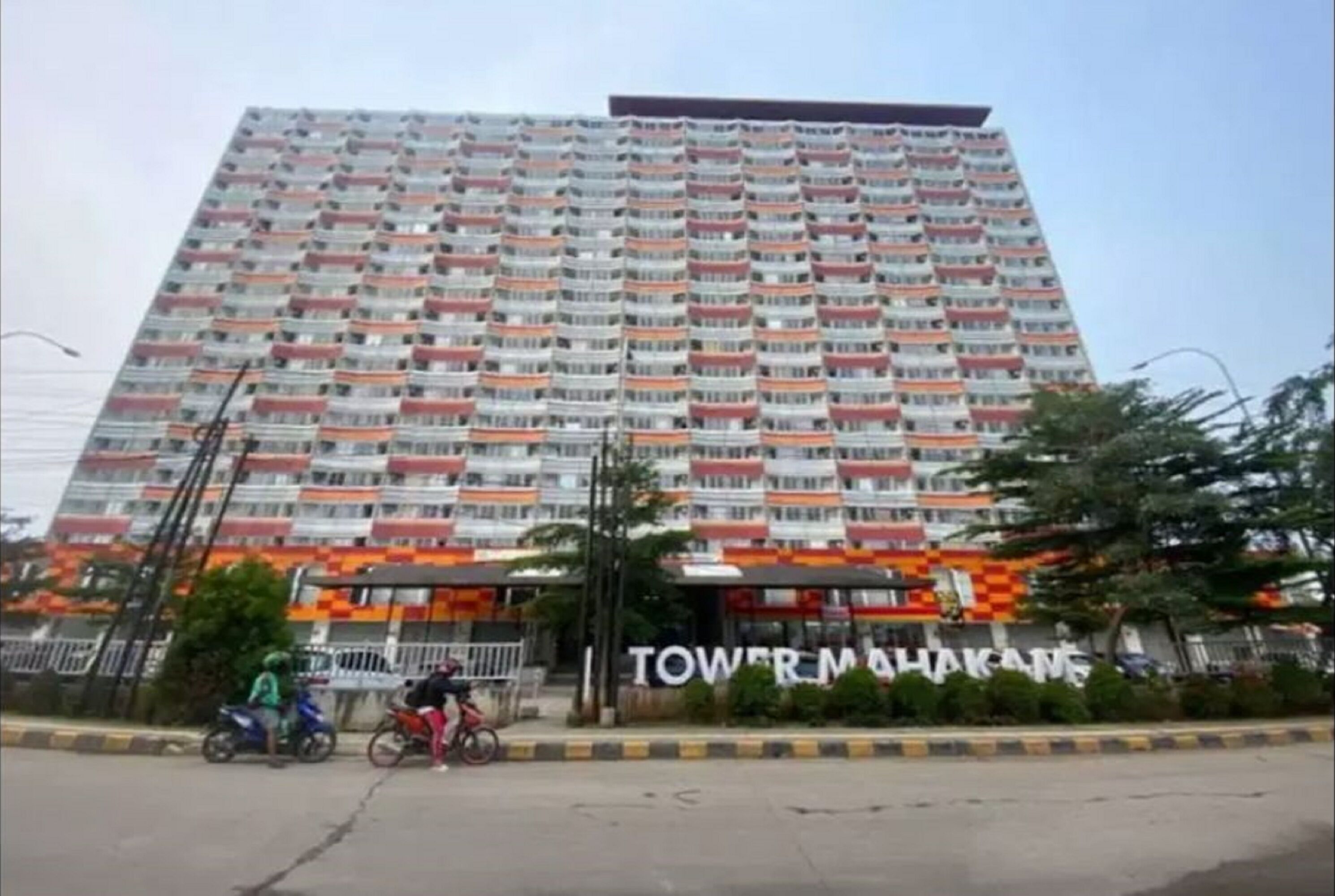 A multi-story hotel with balconies, a sign reading "TOWER MAKAS," and a street with cyclists.