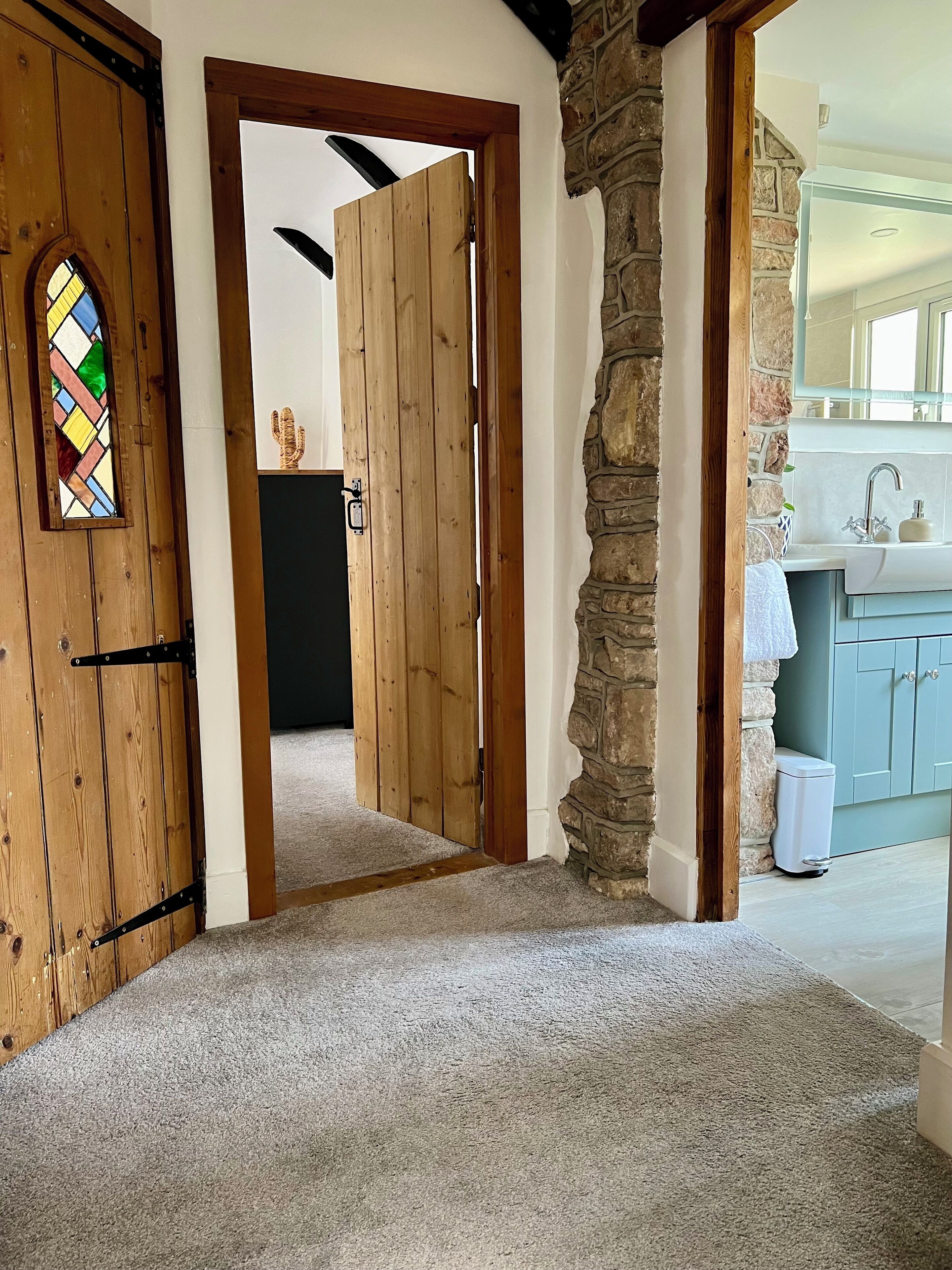 A hallway leading to a bathroom with a stone wall, a wooden door, and a stained glass window.