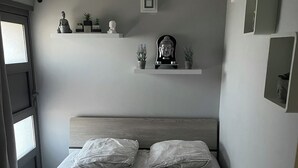Ein Schlafzimmer mit einem Bett, zwei Kissen, einem Kopfteil, einem Fenster und einer Tür.