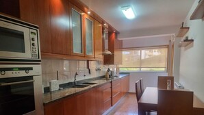 Cozinha com armários de madeira, forno embutido, pia e área de jantar com mesa e cadeiras.