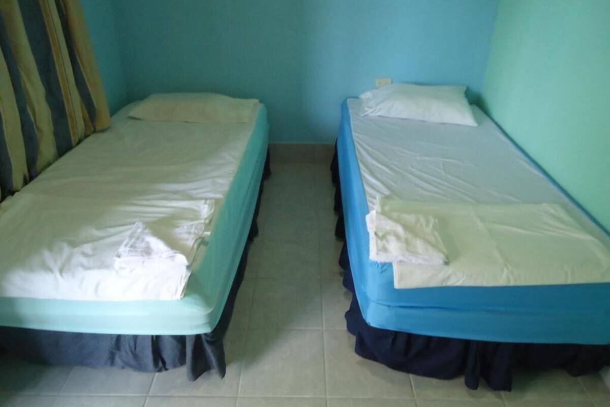 Due letti singoli con lenzuola bianche, una parete blu e una tenda a sinistra.