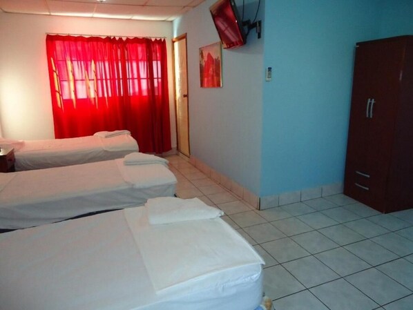 A hotel room with two single beds, a red curtain, a television mounted on the wall, and a wardrobe.