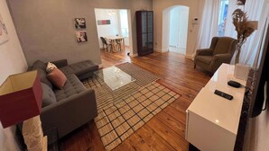 Un salon moderne avec un canapé gris, une table basse et un meuble pour la télévision. On aperçoit à l’arrière-plan un coin repas avec une table et des chaises.