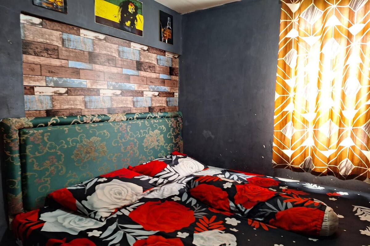Een slaapkamer met een bed met een geborduurd sprei, een hoofdbord met een bloemenprint, een metselwerk muur en een geometrisch gordijn.