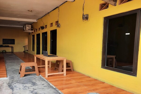 Ein Zimmer mit gelber Wand, einem großen Fenster und einem Holztisch mit zwei Hocker.