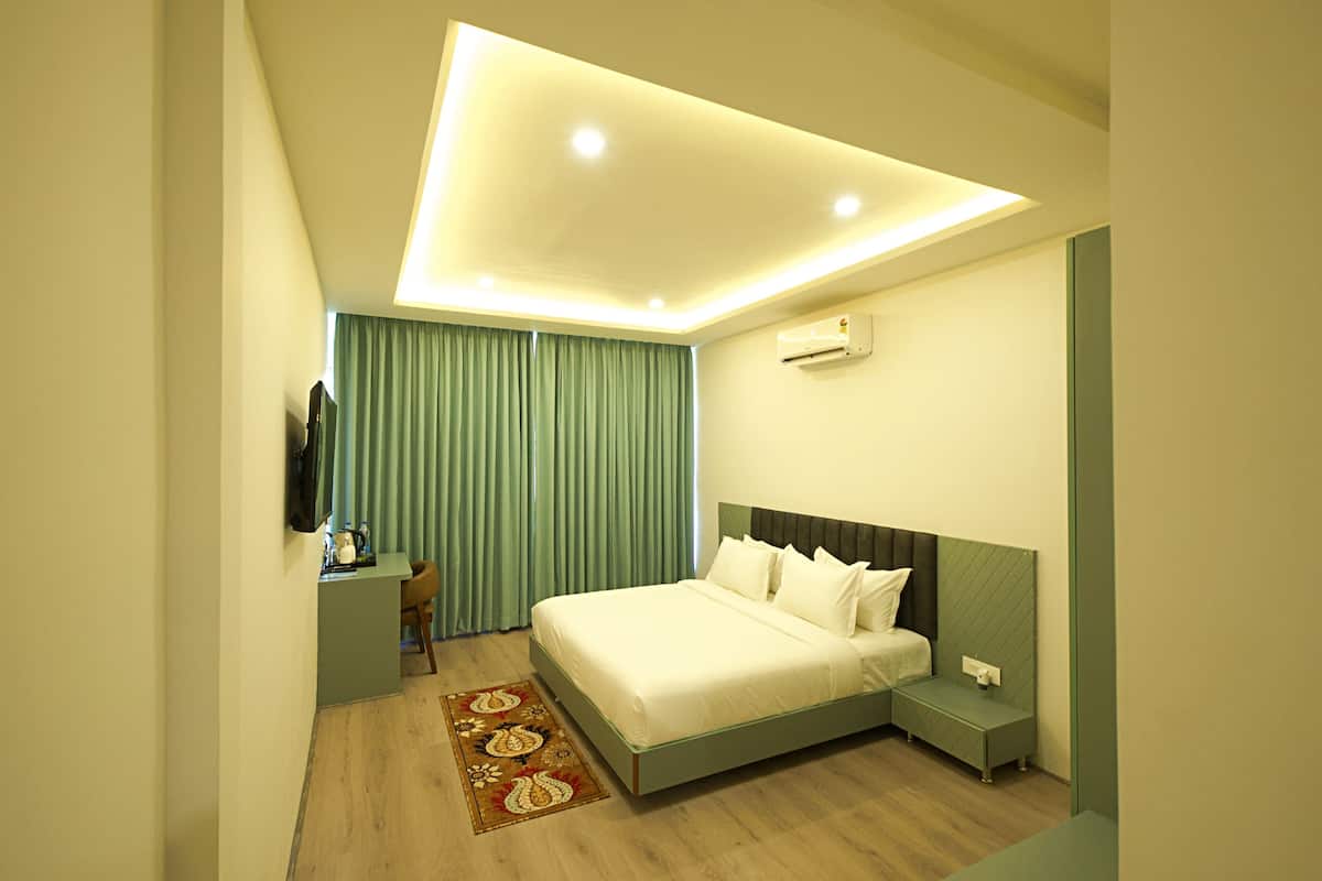 A modern hotel room with a large bed, bedside table, and a desk with a chair.