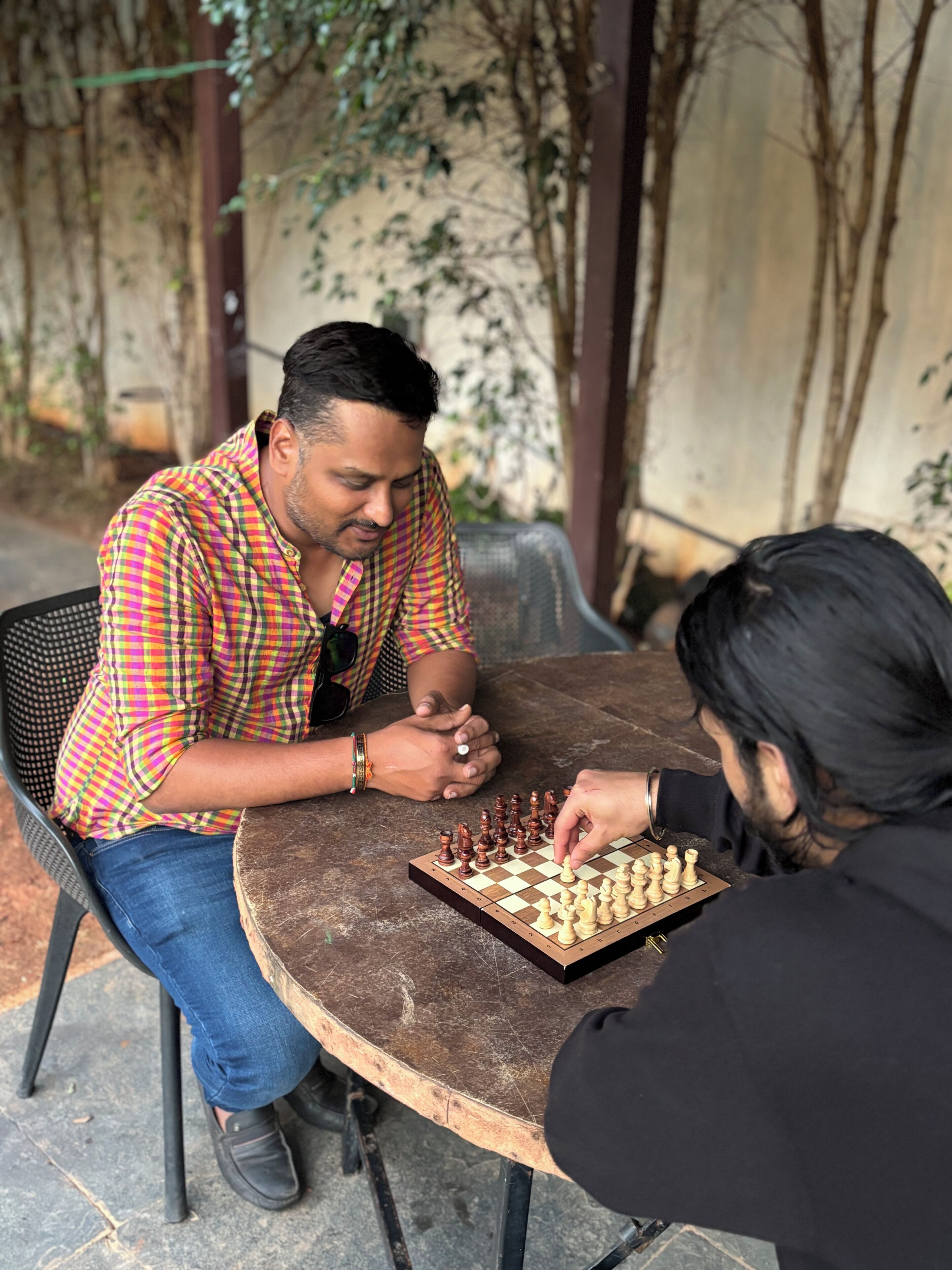 Dos personas jugando ajedrez en una mesa al aire libre.