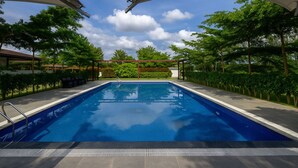 Une piscine rectangulaire à l’eau d’un bleu limpide, entourée d’une terrasse dallée et ombragée par de grands parasols blancs.