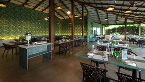 Un restaurant spacieux avec de hauts plafonds, des poutres apparentes et un mur végétal luxuriant. Les tables sont dressées avec des nappes blanches et décorées de centres de table.