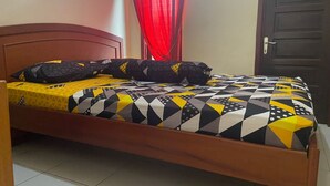 A bed with a patterned bedspread and pillows, a wooden headboard, a red curtain, and a closed door.